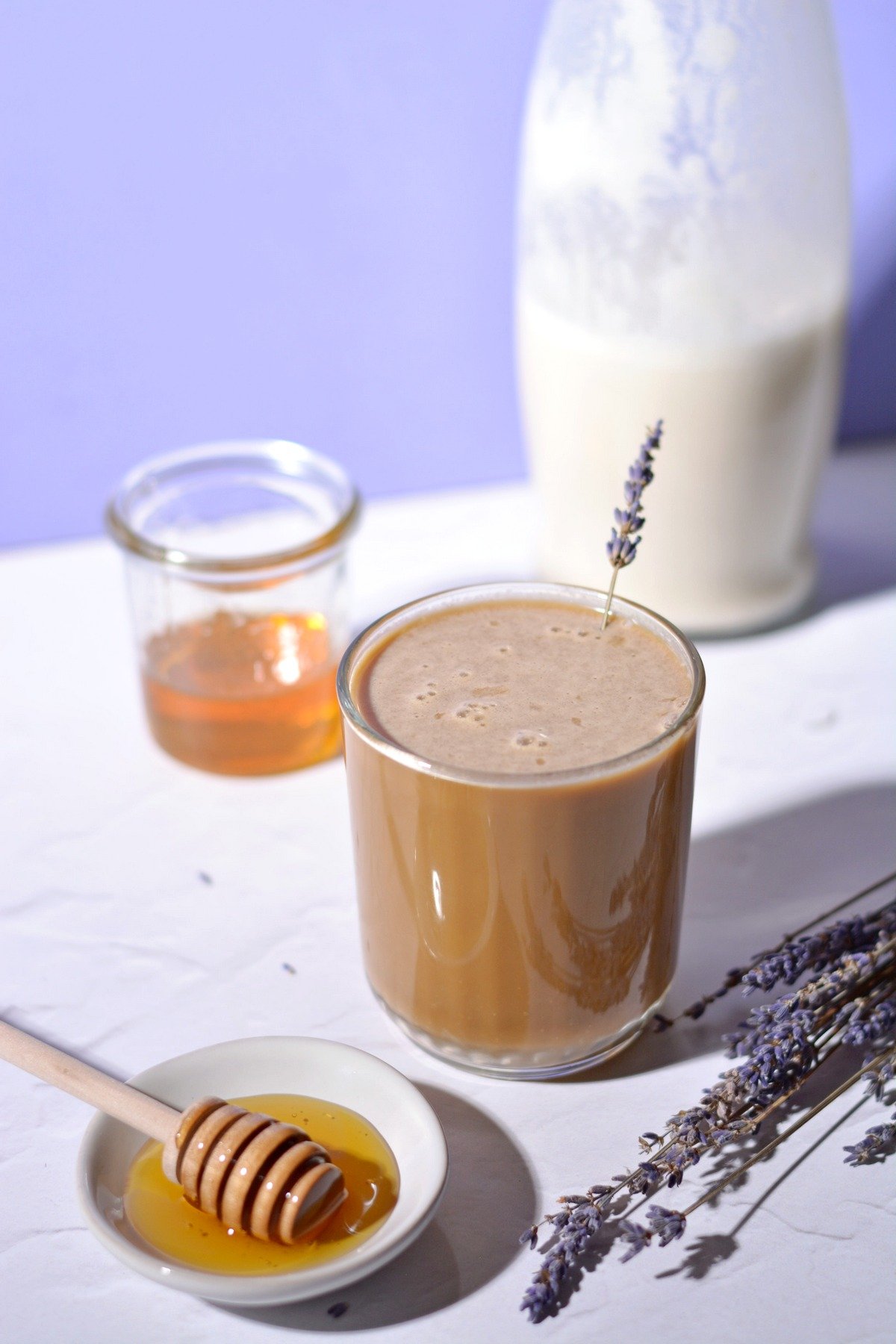 A honeybee latte in a glass with a sprig of lavender surrounded by honey.