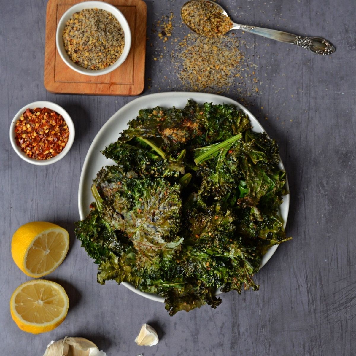 Kale chips on a plate with lemon and spices next to it.