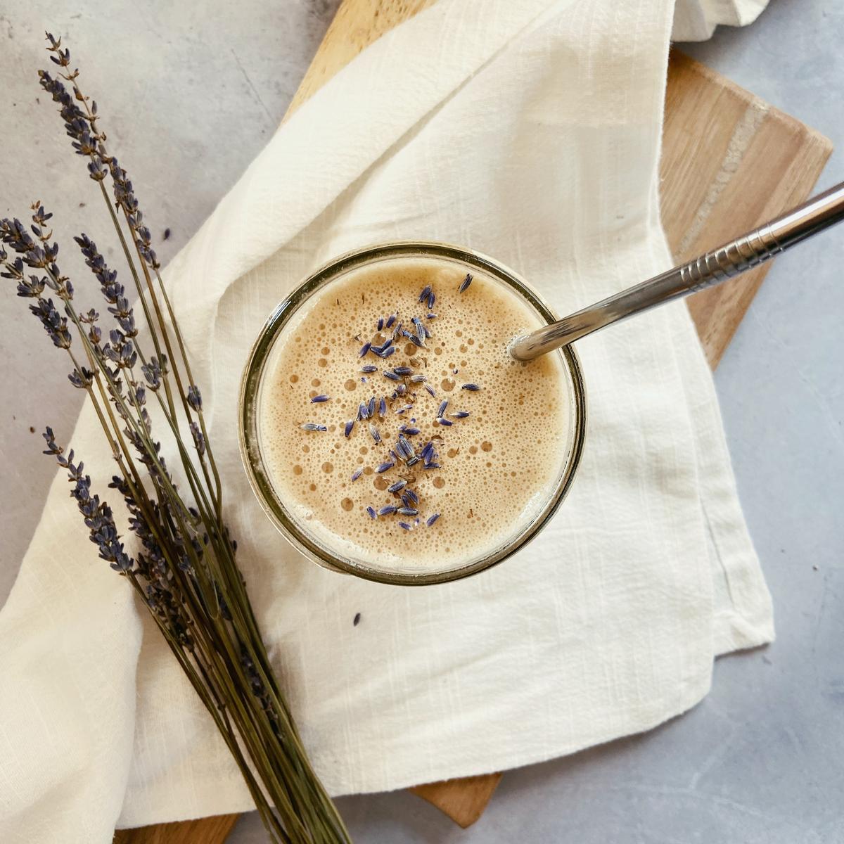 Overhead view of honey lavender latte in a glass cup with lavender buds on top.