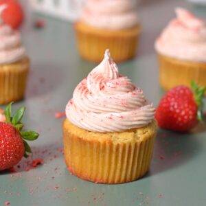 Protein vanilla cupcake with strawberry frosting on a green background next to strawberries.