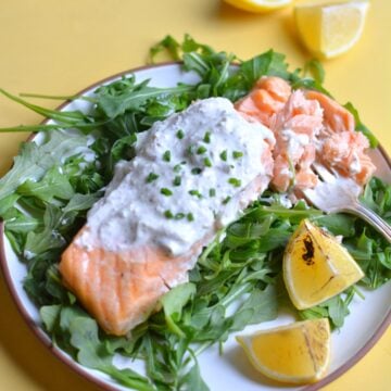 A plate of greens with salmon on top with whipped feta on top.