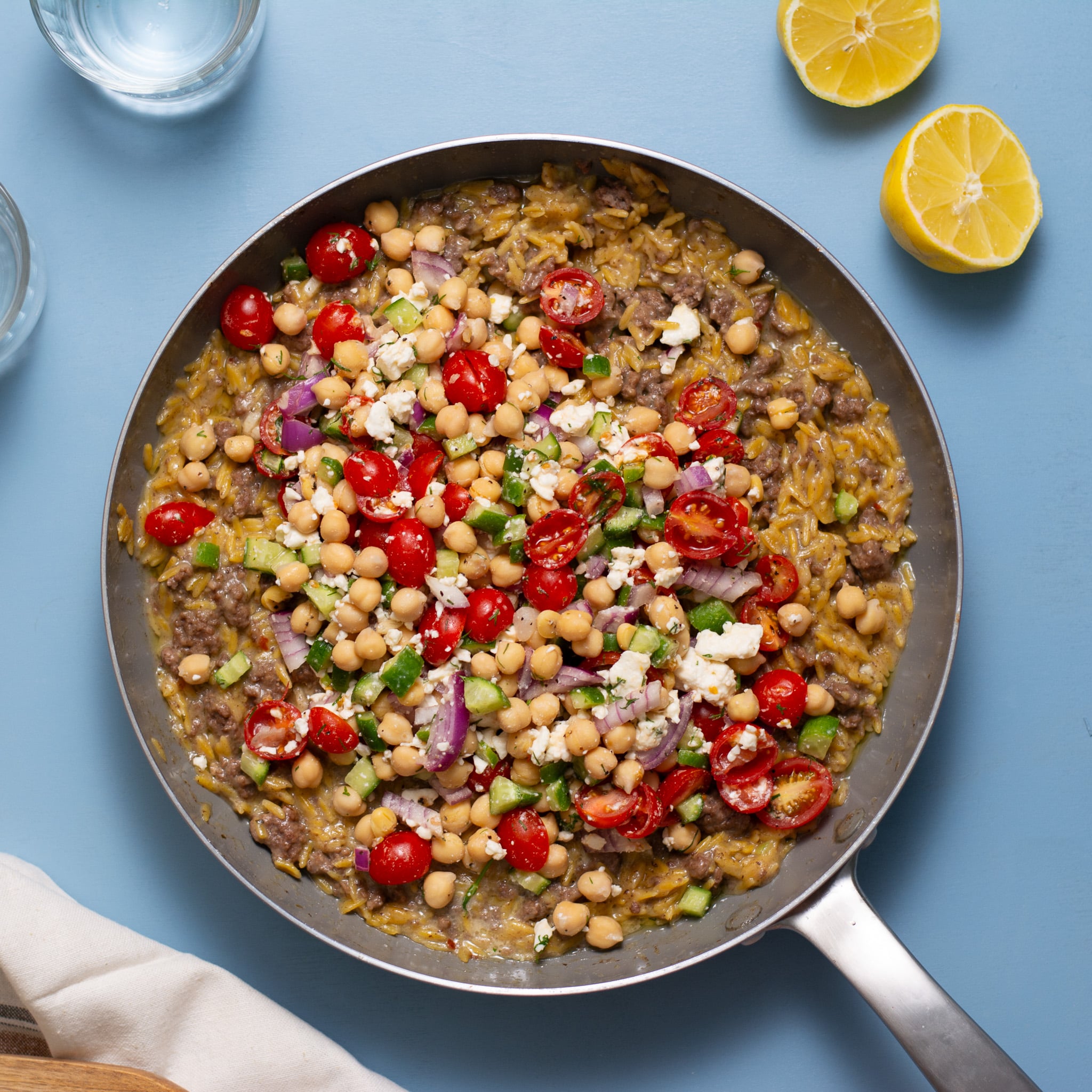 gyro casserole in a skillet on a blue background with a tomato salad on top.