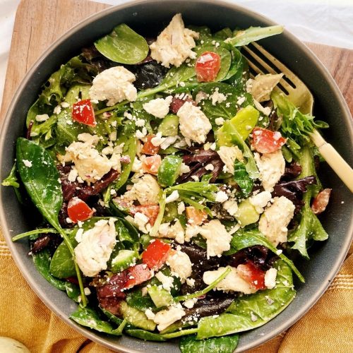 Spinach salad with chicken, tomatoes and olives on top.