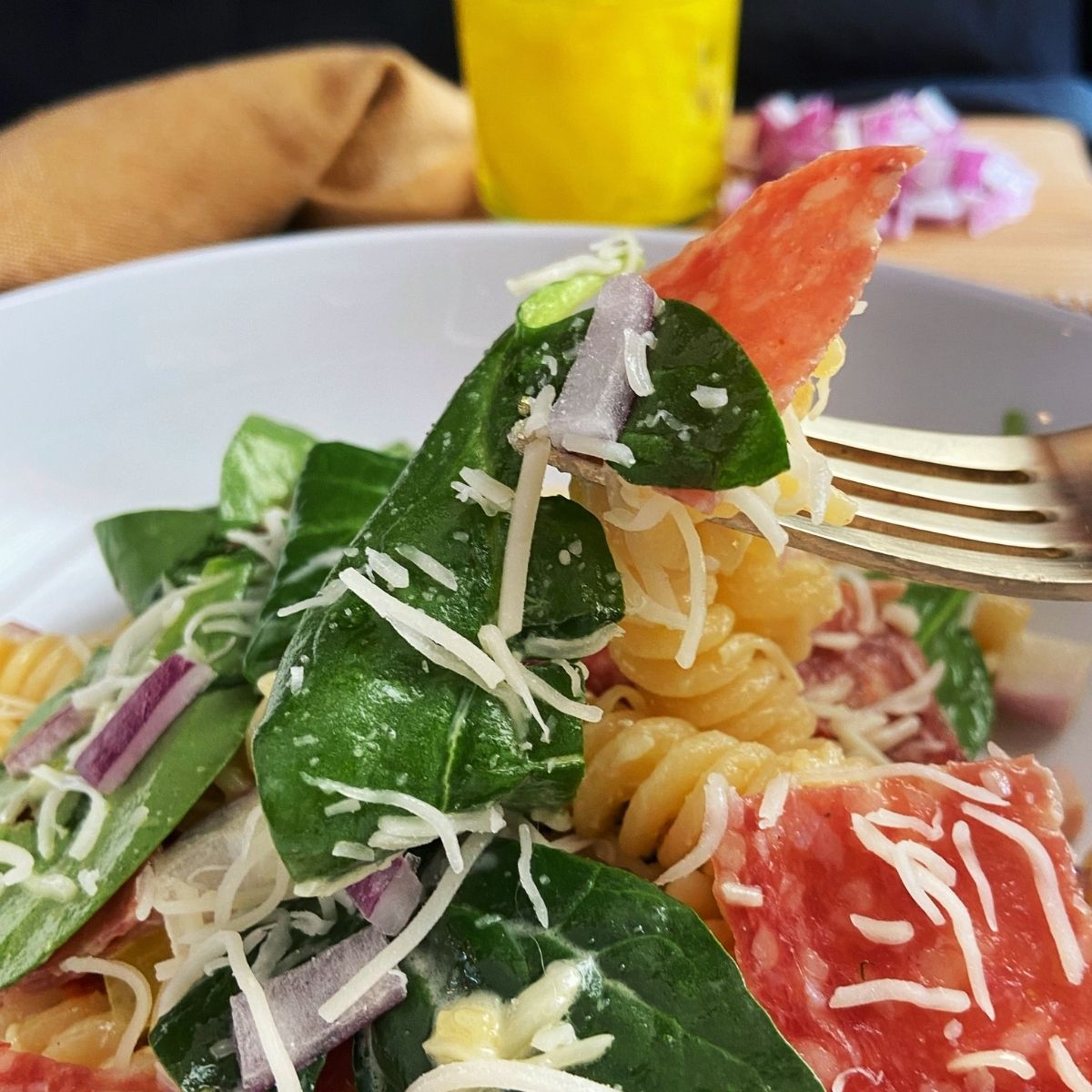 A fork taking a bite of pasta with spinach and pepperoni.