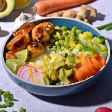 Chicken poke bowl with avocado, radishes, limes, edamame, cucumber, carrots, and mango sauce.