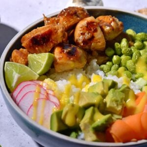 Chicken poke bowl with avocado, radishes, limes, edamame, cucumber, carrots, and mango sauce.