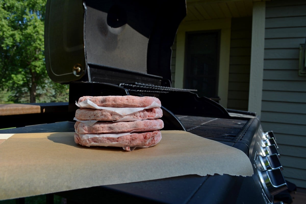 Stack of burgers on parchment paper next to an open grill.