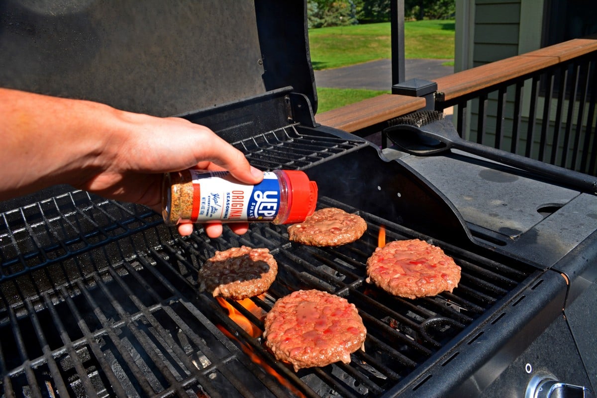 Sprinkling seasoning on top of burgers on a grill.