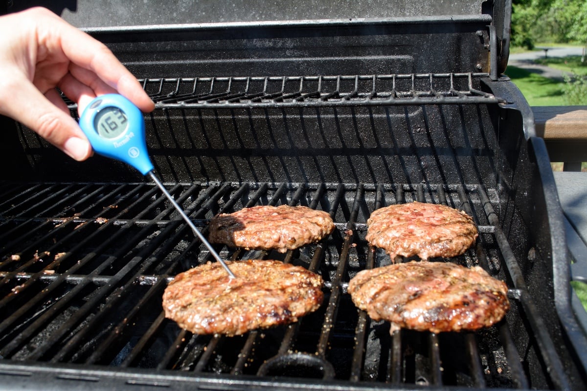 Checking the temperature of burgers on a grill.