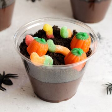 A dirt cup with a layer of chocolate pudding, crushed oreos, and gummy worms and pumpkin candy.