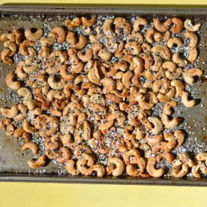 Roasted cashews on a tray with seasoning on them.