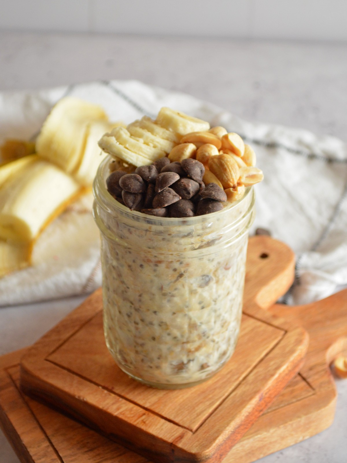 Close up of oats in a glass mason jar with chocolate chips, peanuts, and bananas on top.