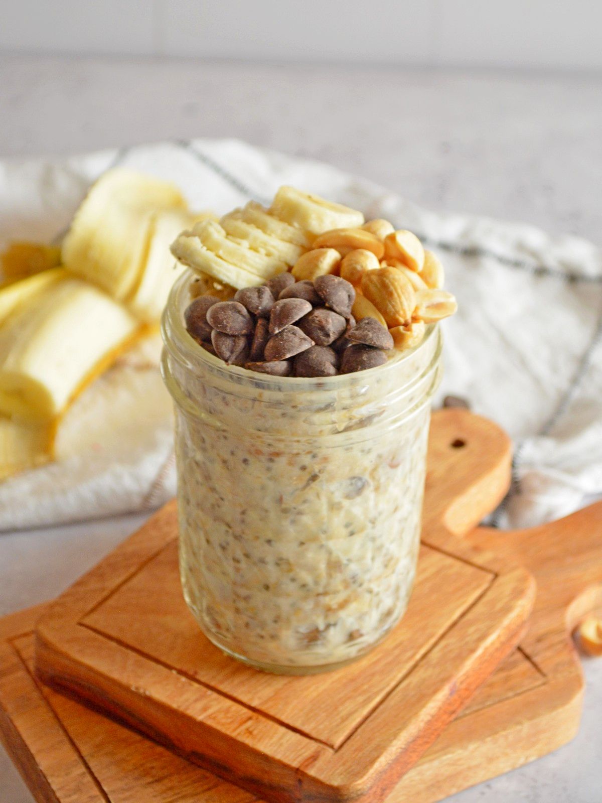 Glass mason jar with chocolate chips, peanuts, and bananas on top of oats