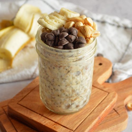 Oats in a glass mason jar with chocolate chips, banana slices, and peanuts on top.