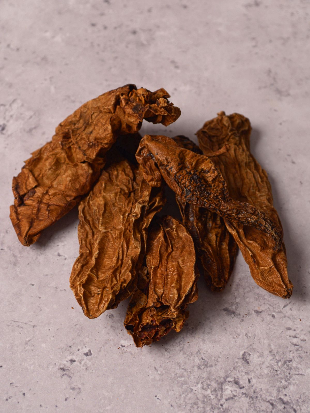 A pile of chipotle peppers laying on a gray table.