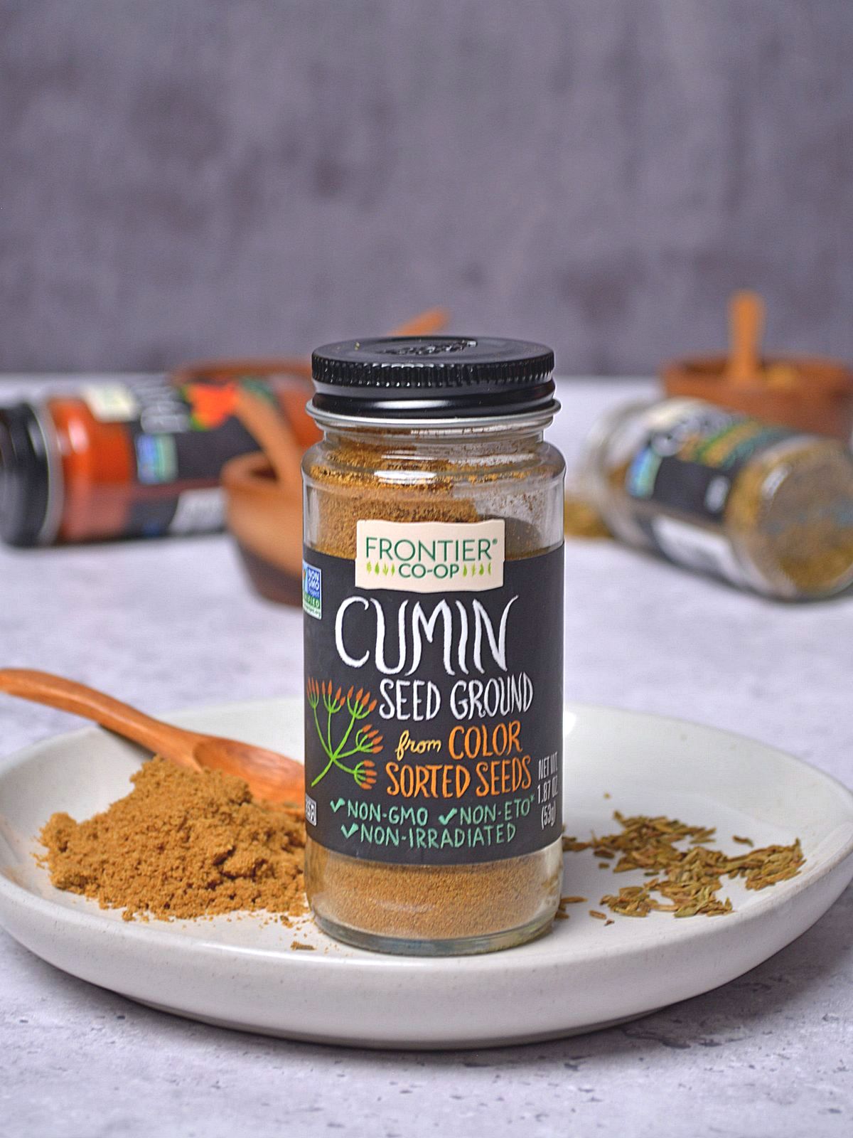 Cumin in a spice jar set on a white plate with ground cumin on the plate