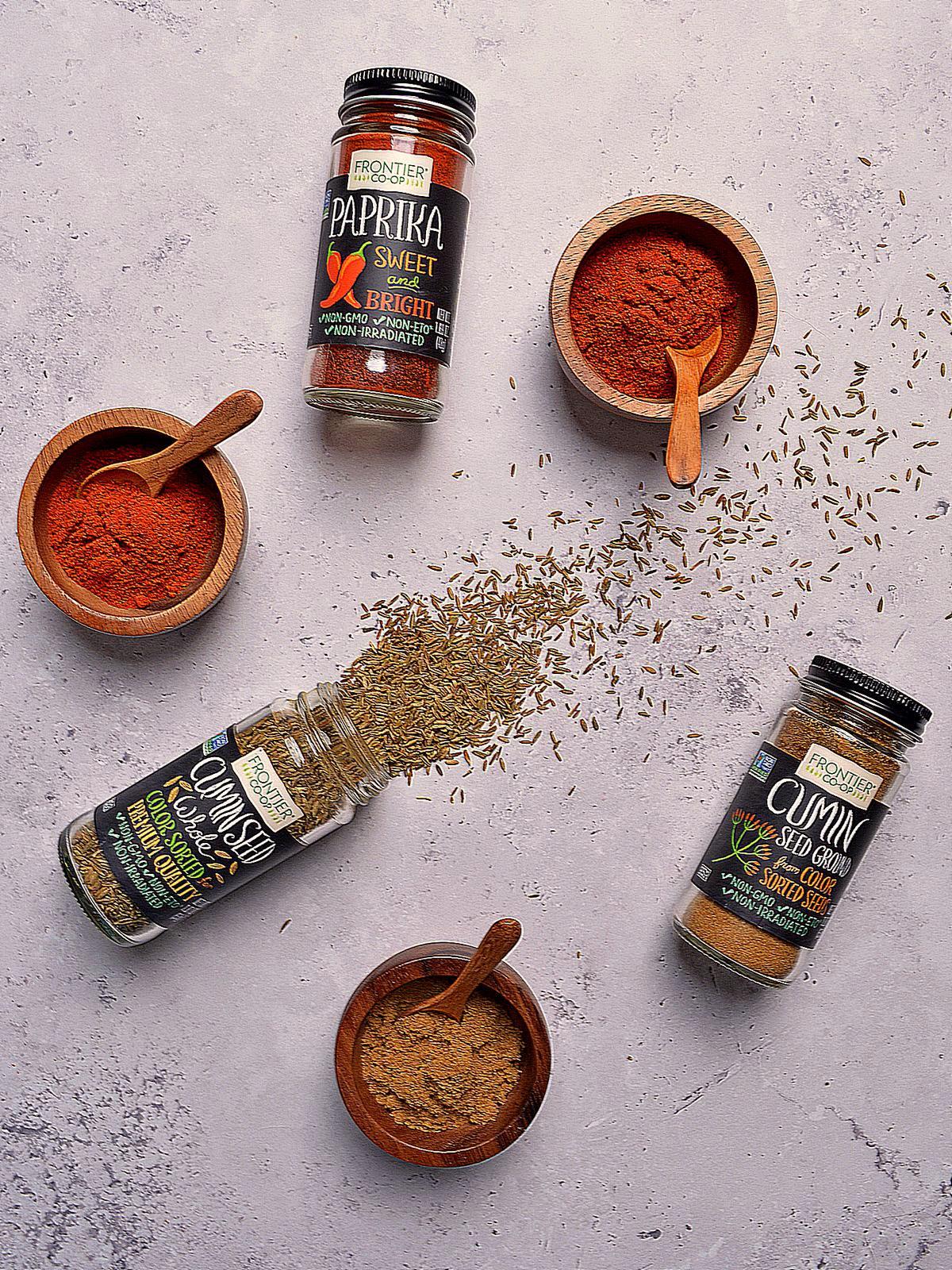 Overhead of cumin and paprika in glass jars and wooden bowls