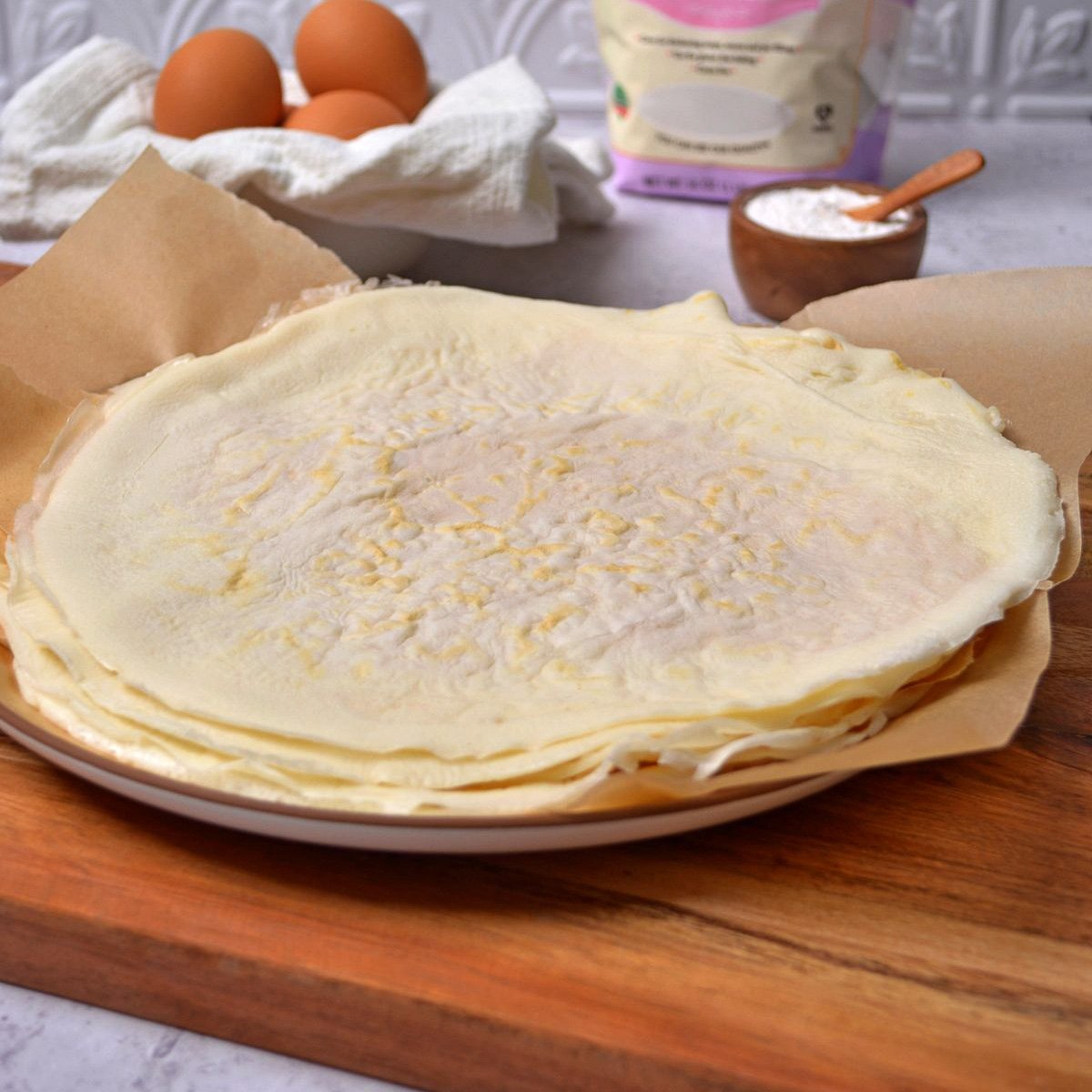 Egg white wraps in a stack with eggs and flour in the background