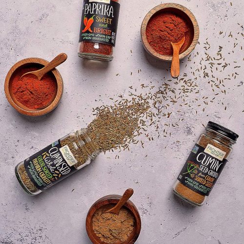 Cumin and paprika in bottles and bowls spread out on a concrete table.