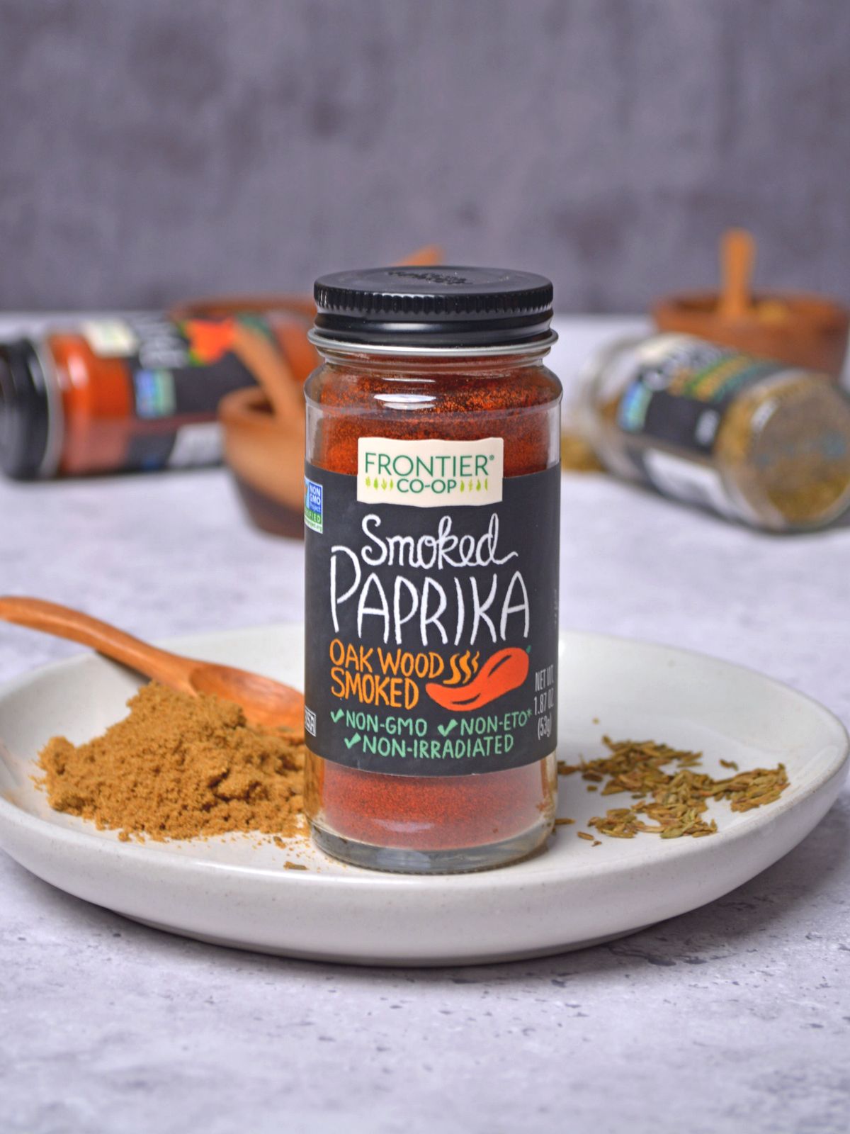 Paprika in a spice jar set on a white plate with ground paprika on the plate