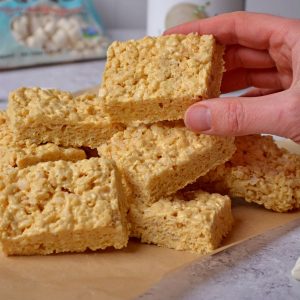 A pile of rice krispies treats with a hand picking one up.