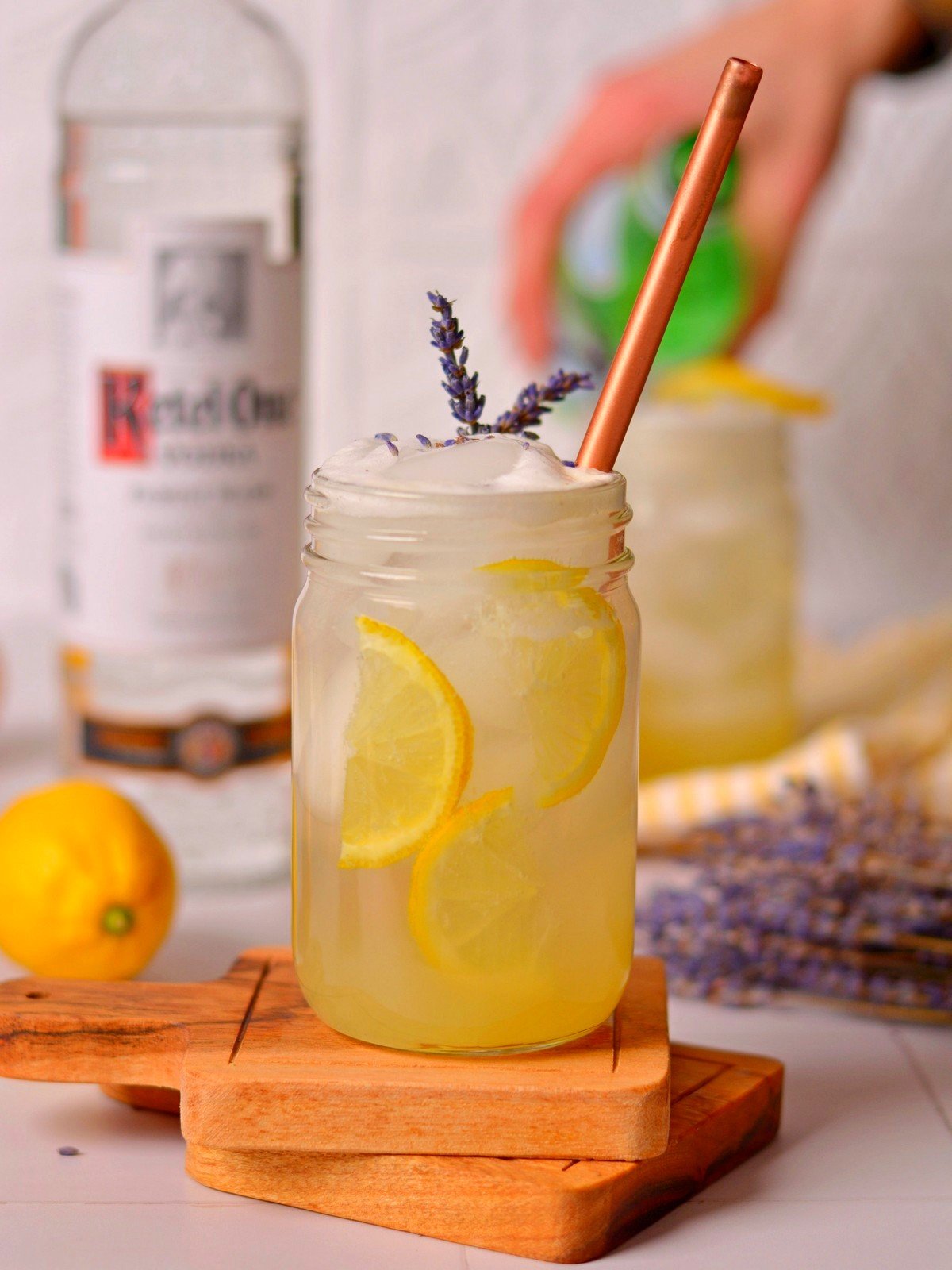 Lavender lemonade vodka cocktail in a glass mason jar with lemon slices, a straw, and dried lavender in the jar.