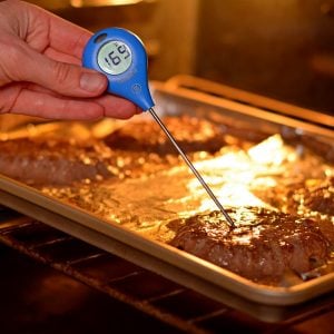 Meat thermometer being held inside a burger patty inside the oven.
