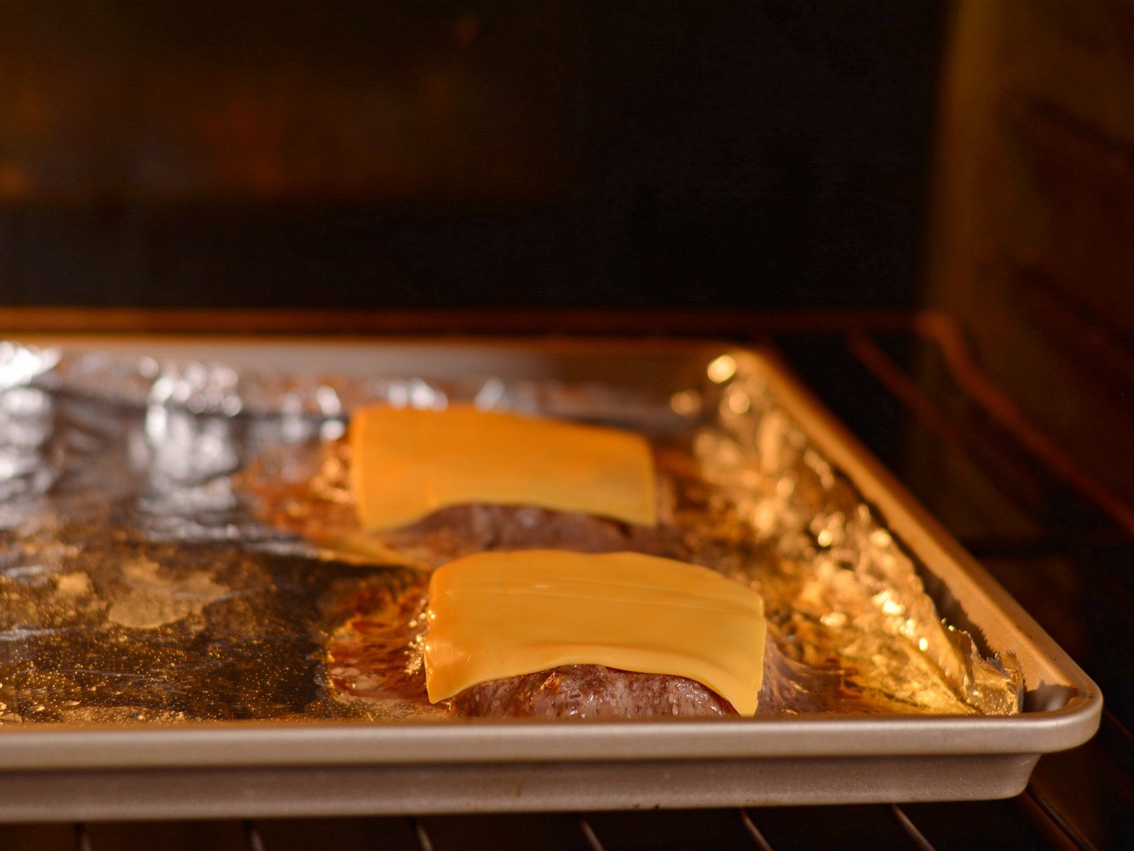 Two burgers with cheese on top of a baking sheet in the oven.