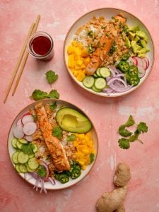 Salmon on top of white rice with cucumbers onion, mango, radish, and jalapenos in a large white bowl.