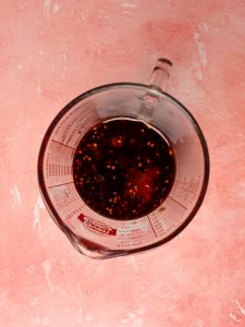 A brown liquid inside a glass measuring cup on a pink table.