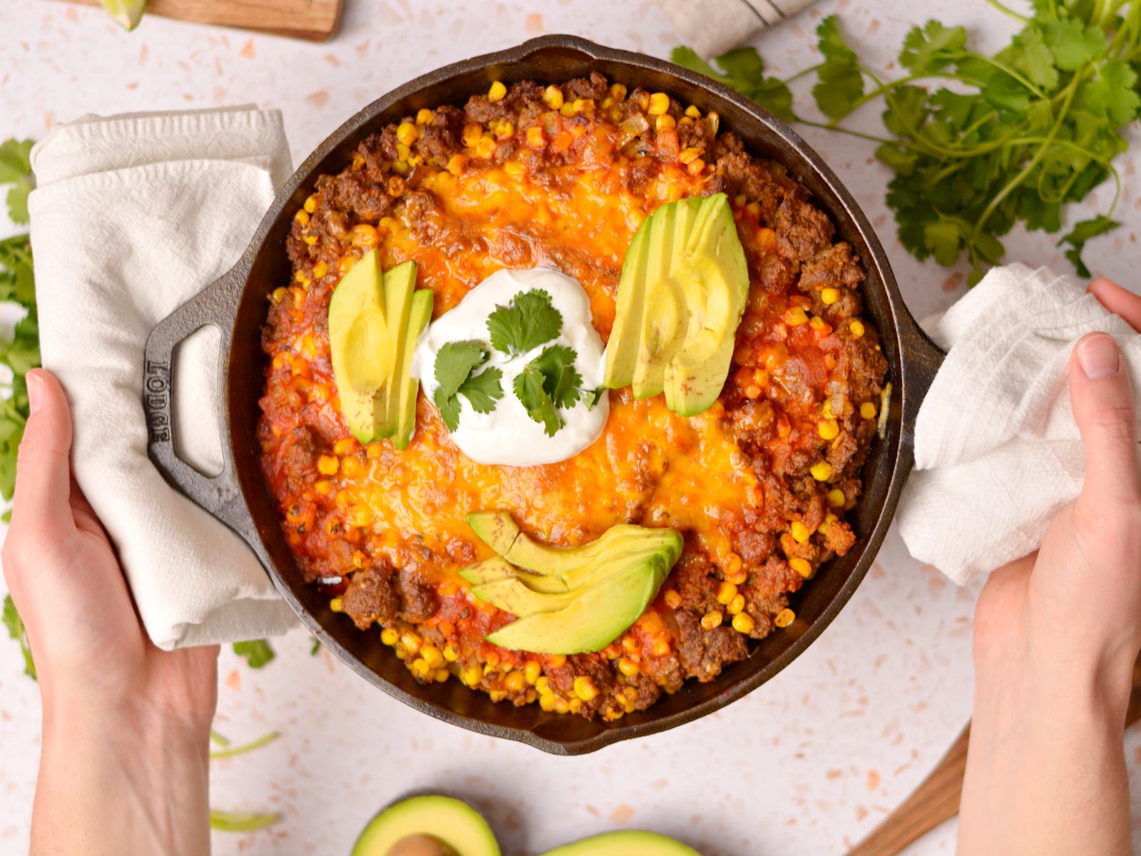 Flat beef enchiladas in a black skillet being set on a concrete table.