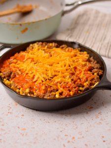 Enchilada mixture with cheese on top in a black skillet.