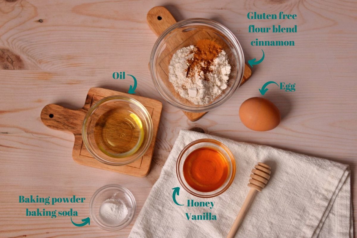 Oil, flour, cinnamon, honey, baking powder, and an egg on a wooden table.