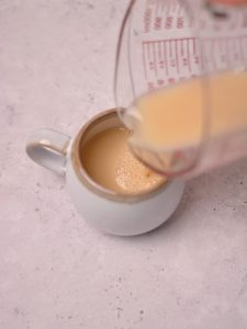 Pouring milk mixture into a cream colored mug.