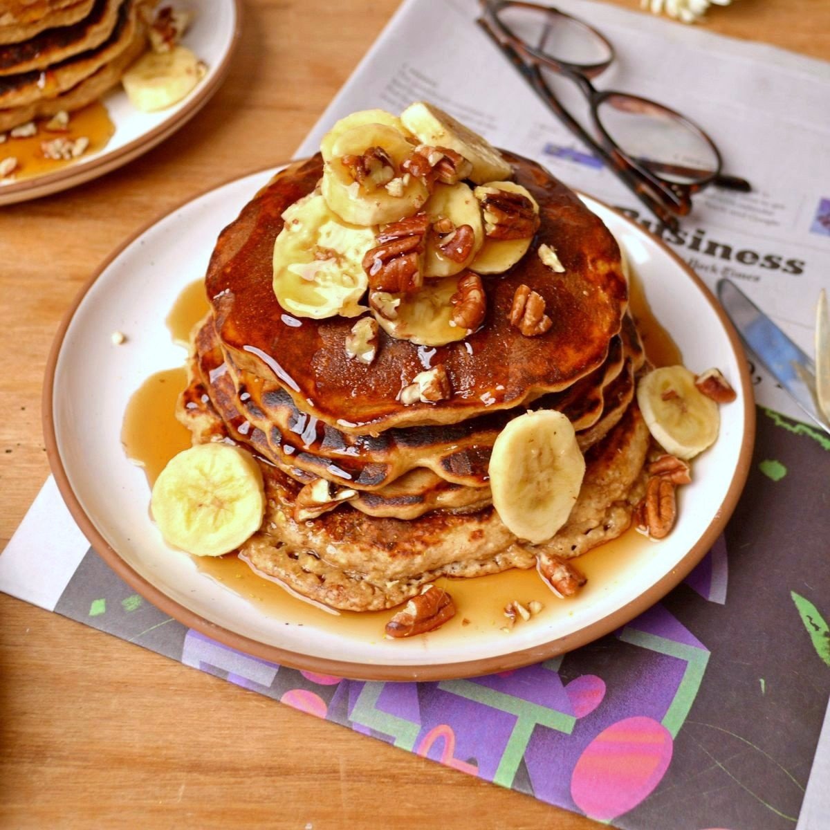 A stack of pancakes with banana slices, pecans and syrup on top.