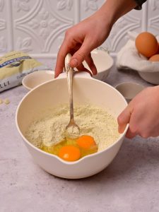 A fork mixing eggs and dry ingredients in a bowl.