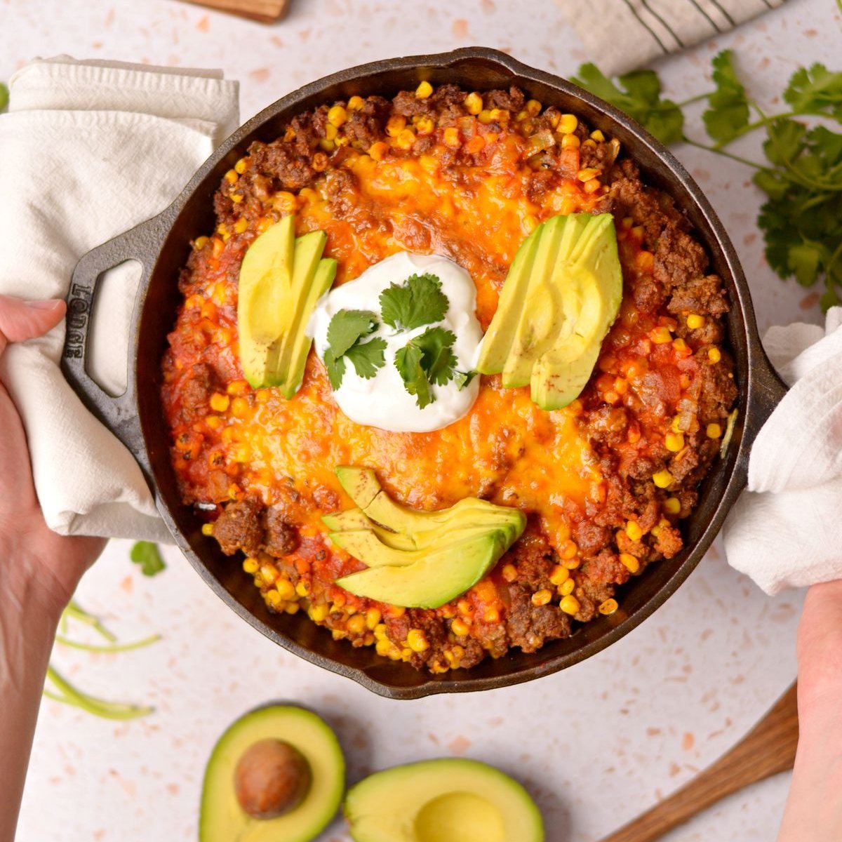 Enchiladas in a black skillet with avocado and sour cream on top.