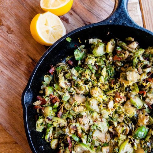 Sauteed brussels sprouts with lemon and bacon inside a black skillet.