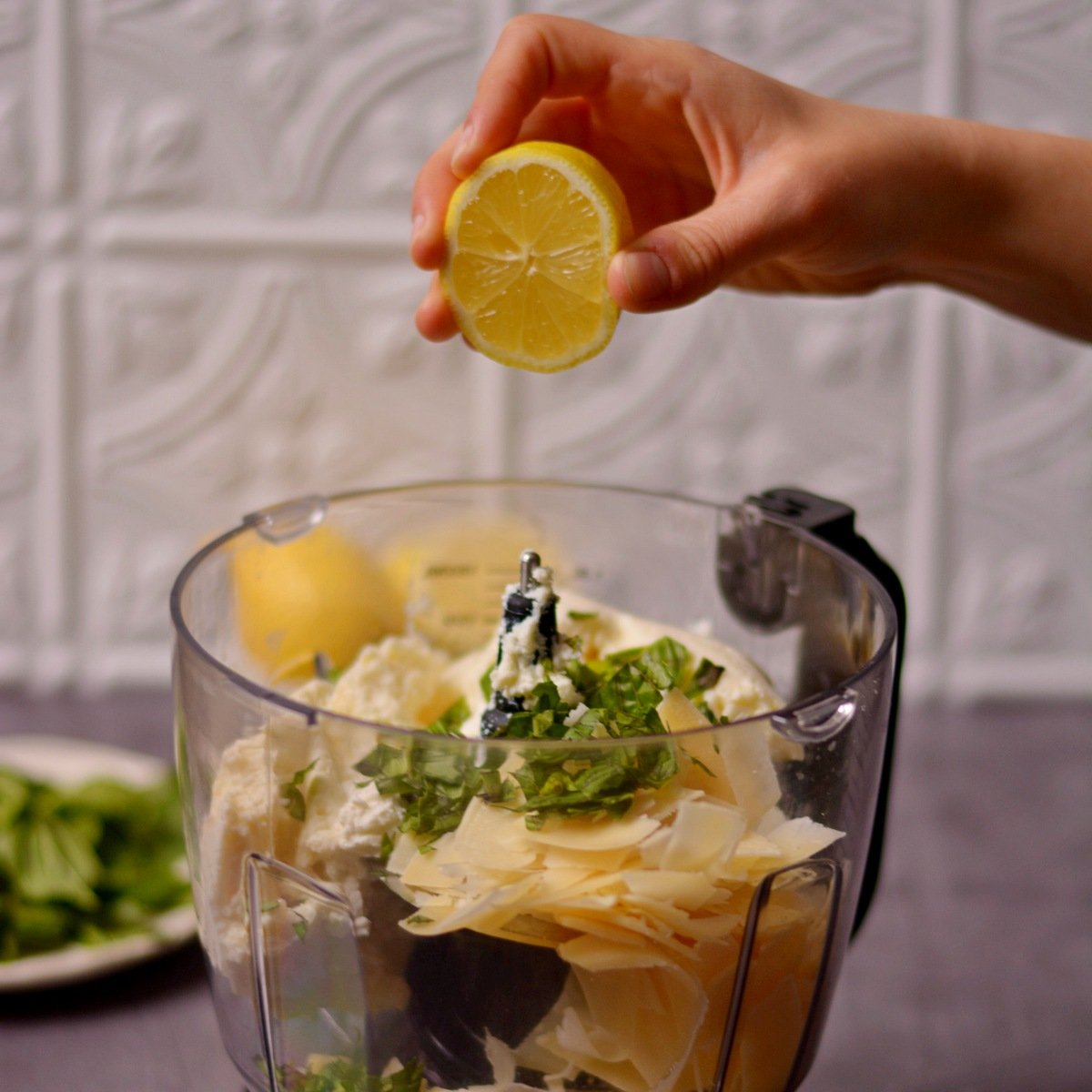 A hand squeezing a lemon over other ingredients inside a blender.