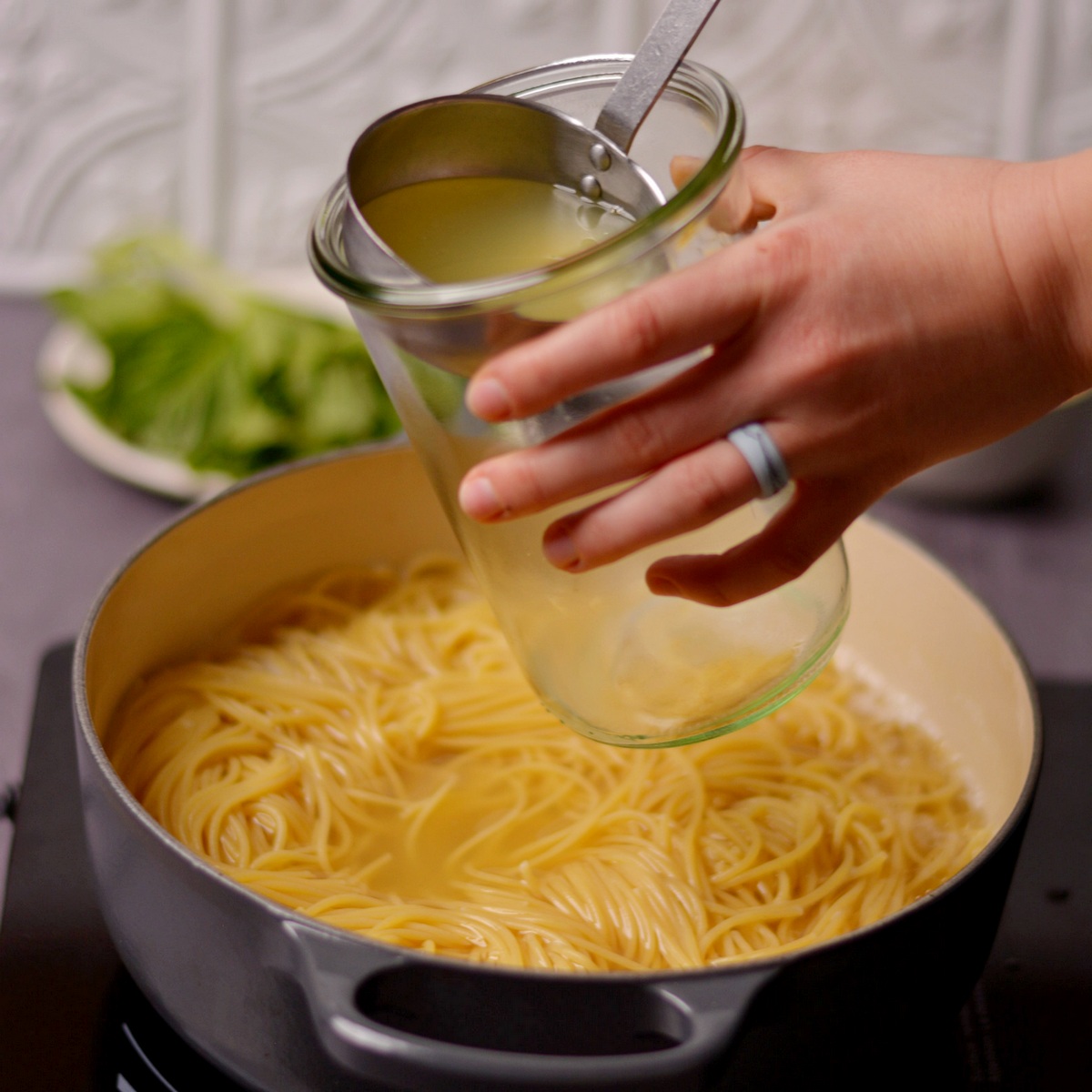 Pouring pasta water into a glass mason jar with a ladle.