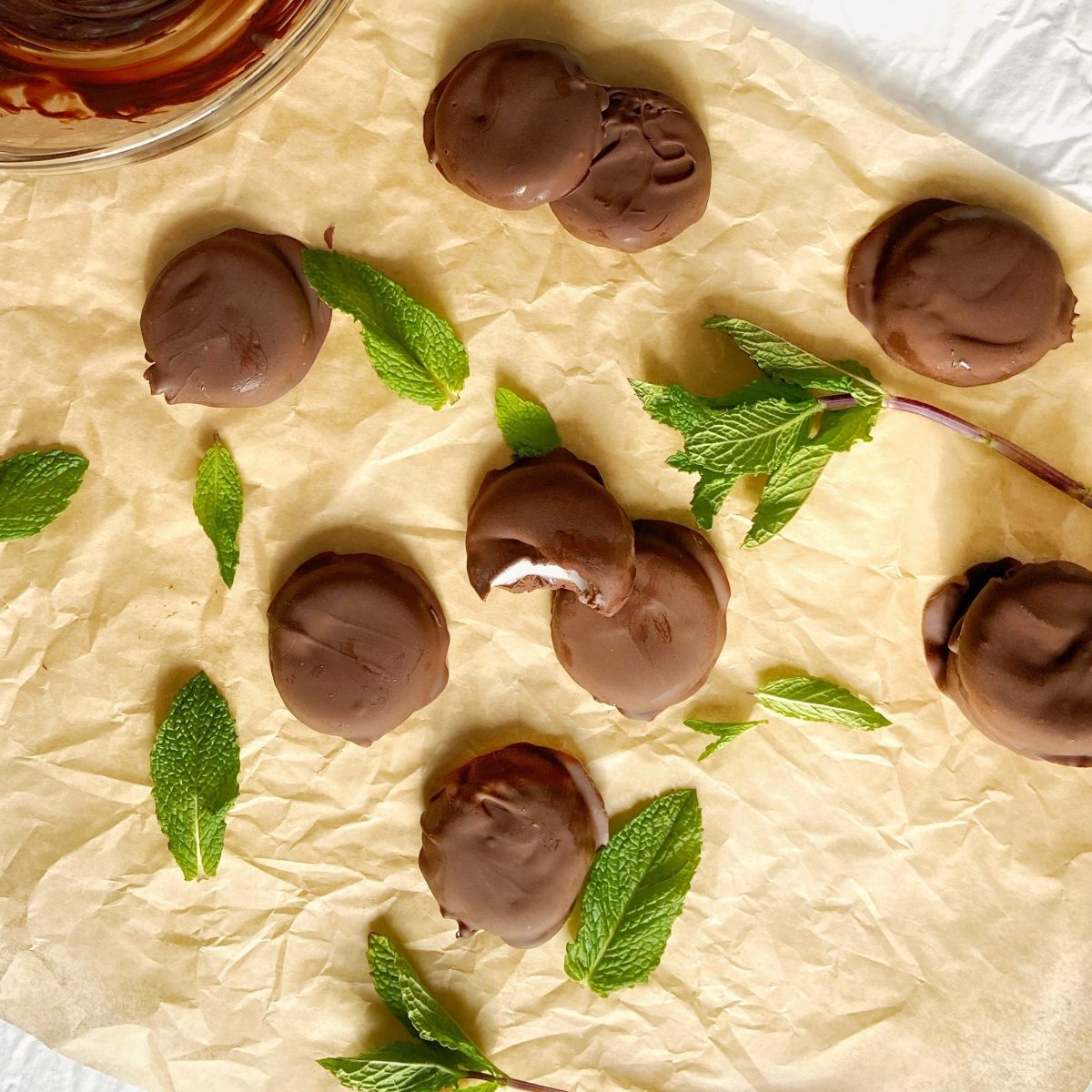 Peppermint patties and fresh mint leaves spread out over parchment paper.
