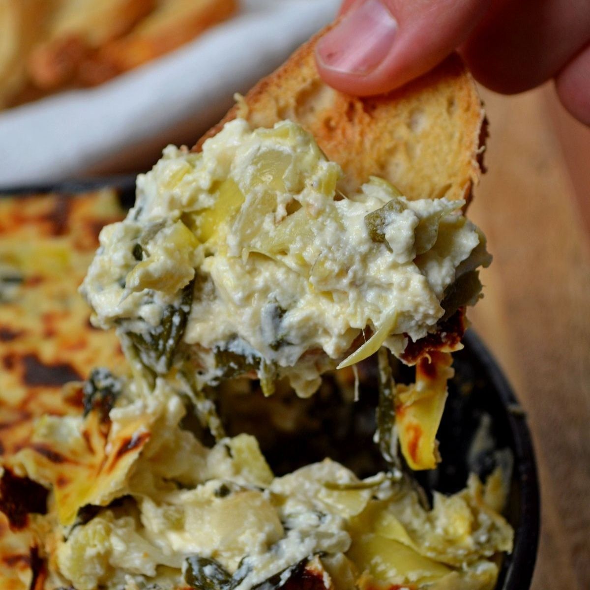 Spinach and artichoke dip in a skillet with bread taking a scoop.