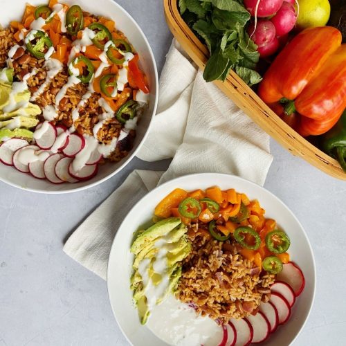 Two bowls filled with rice, yogurt, and various vegetables.