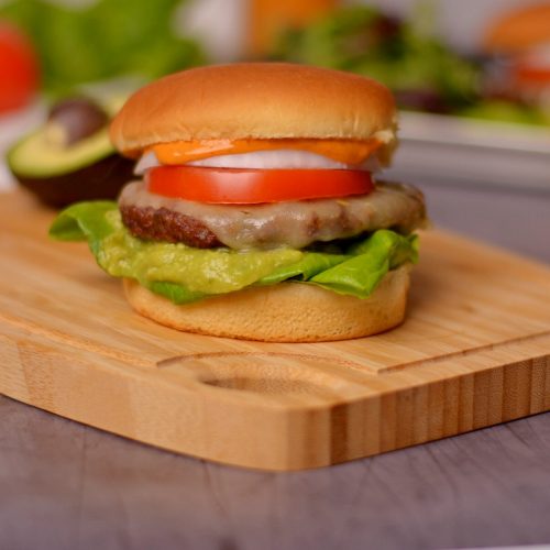 A burger with veggies on it on top of a wood cutting board.