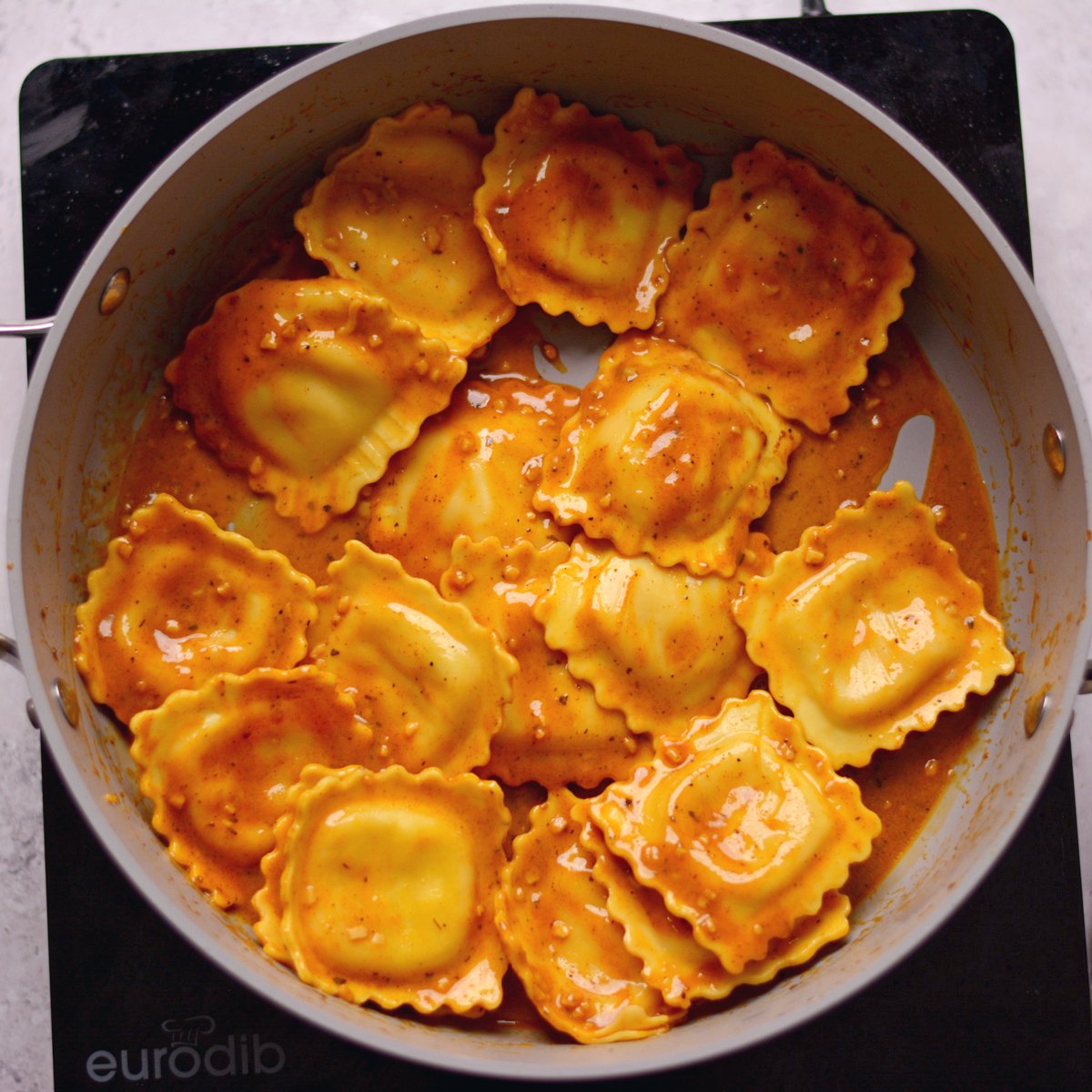Ravioli covered in brown sauce inside a pan.