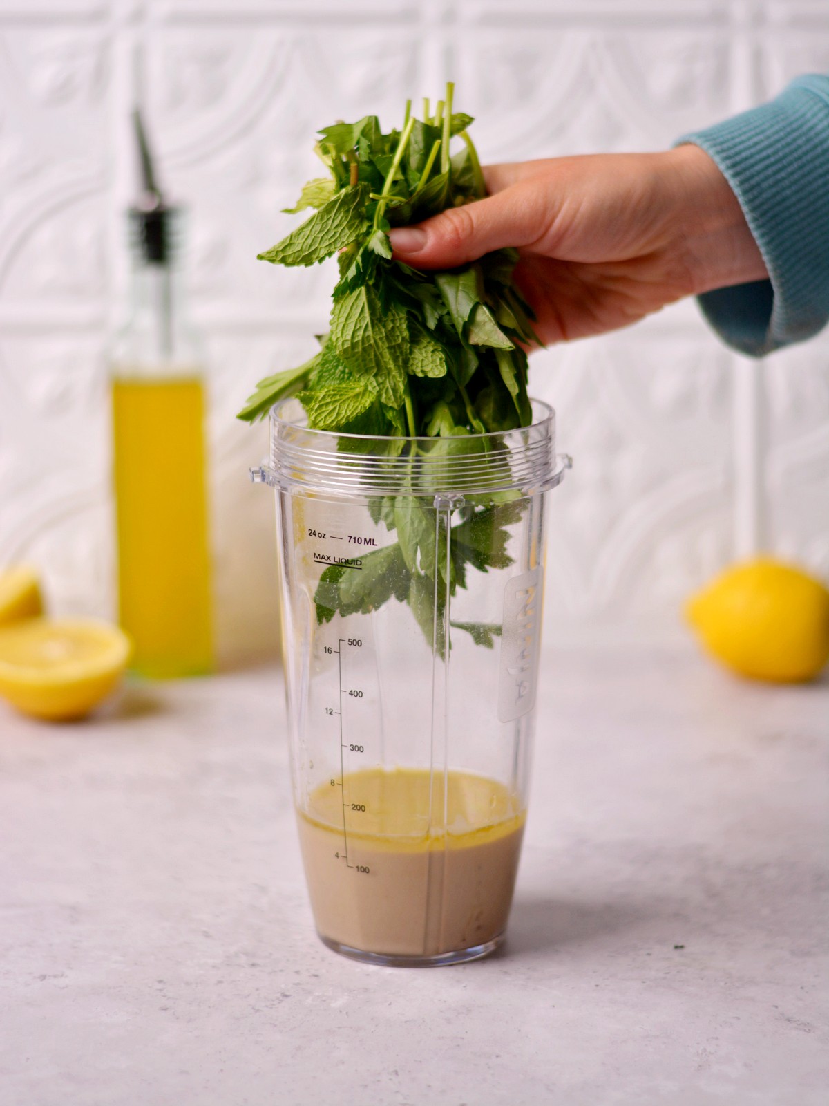 A hand adding herbs to a blender cup.