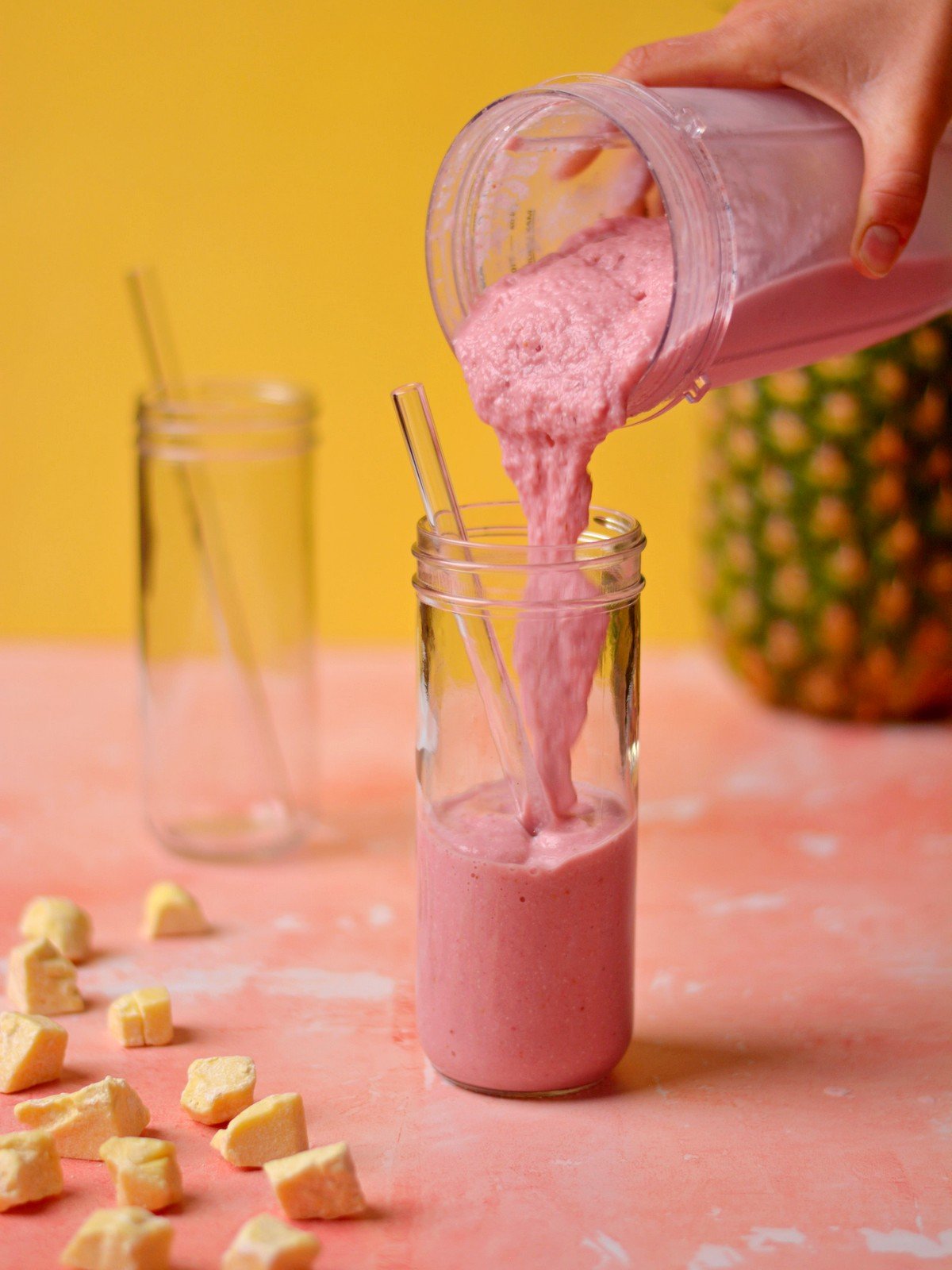 Pouring a pink colored smoothie into a glass with a straw.