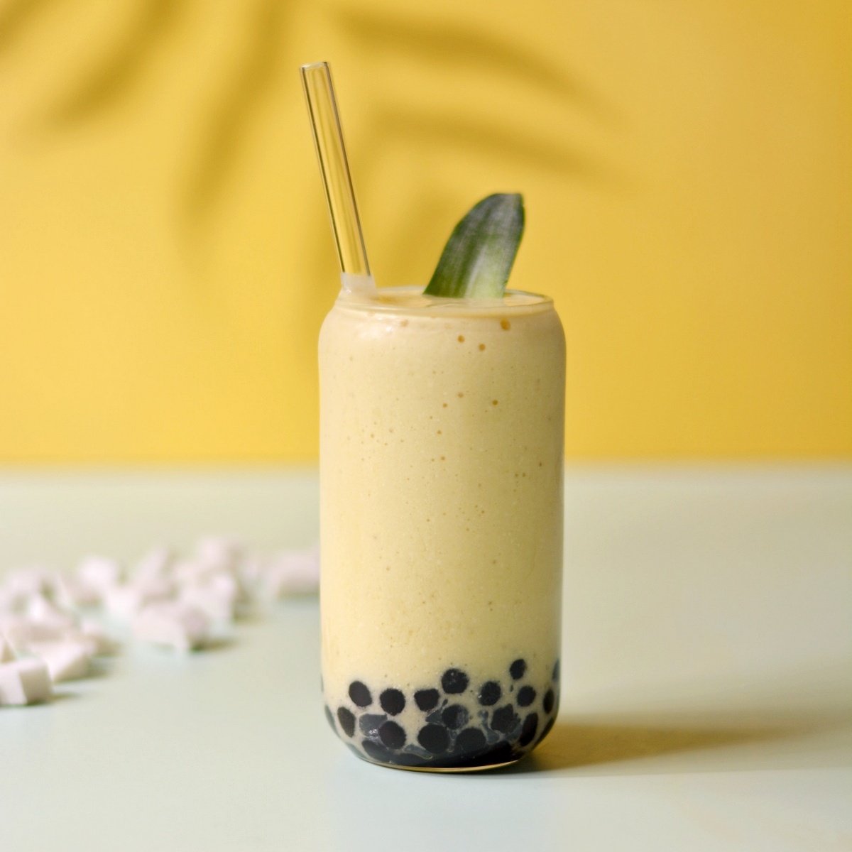 A glass cup with black boba pearls in bottom and yellow smoothie inside.