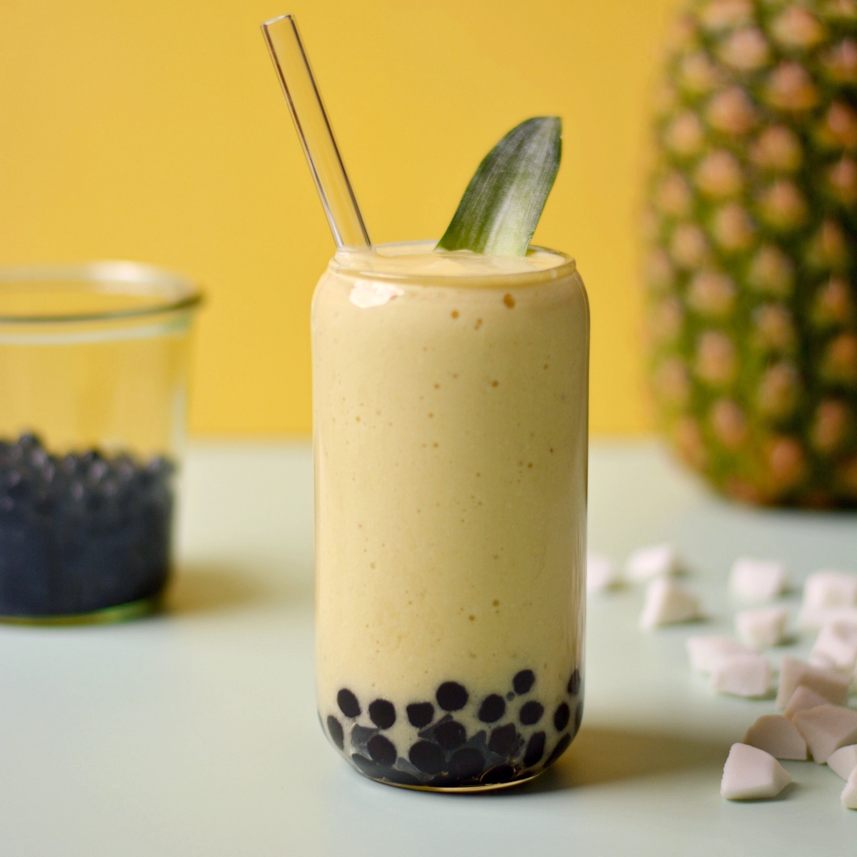 A glass cup with a yellow smoothie inside with black boba pearls in the bottom.
