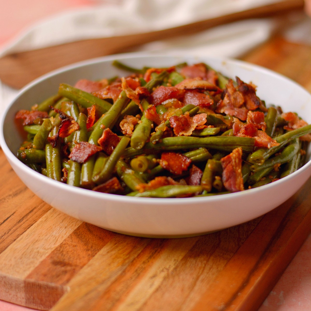 Bacon and green beans inside a shallow white bowl.